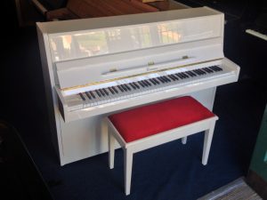 white upright piano with red top stool
